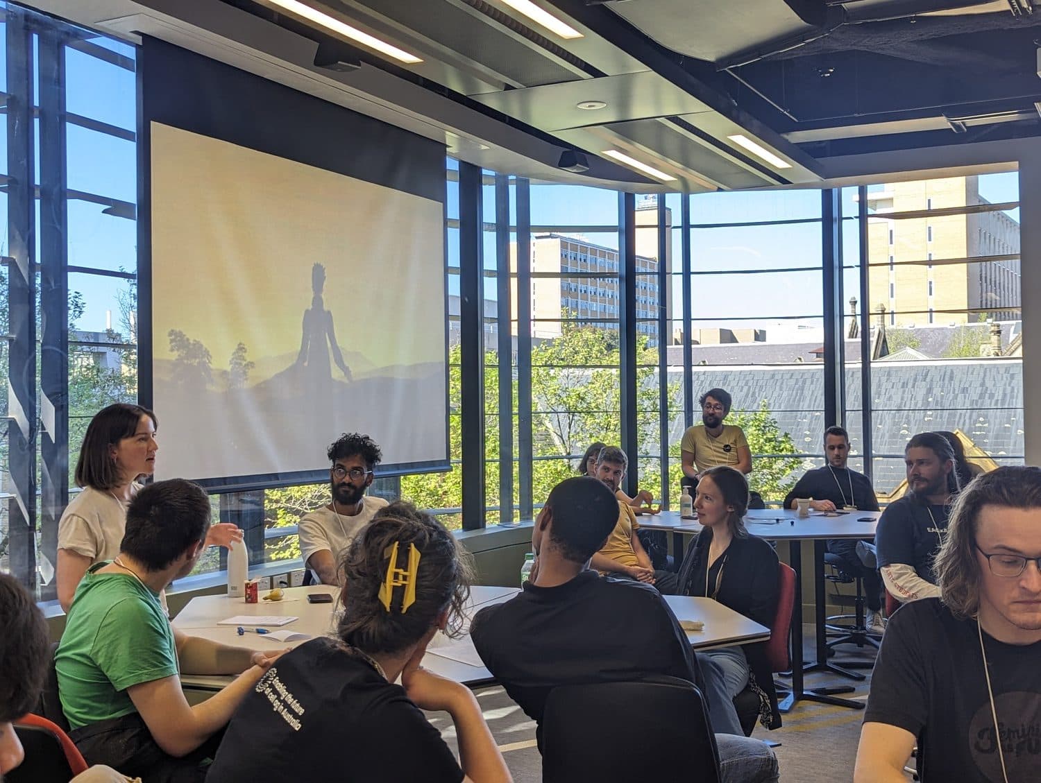 A full room of participants seated at numbered tables, the golden sunset scenario slide projected on the wall.